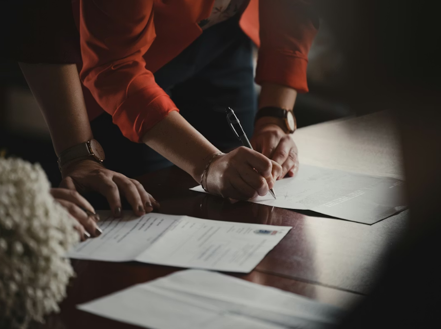 Close-up of a person signing official documents on a desk.